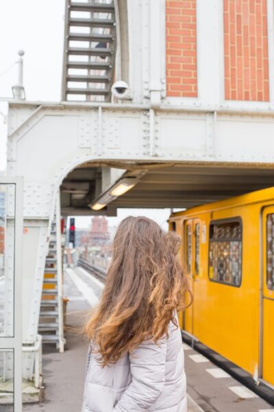 Eine Frau steht auf einer Bahn-Plattform, an der gerade eine Bahn vorbeifährt. 