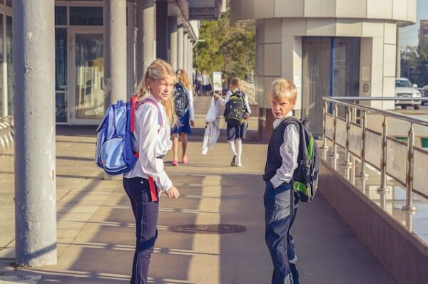 Zwei Schulkinder auf dem Schulweg schauen in die Kamera.
