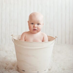 In einem cremefarbenen Eimer sitz ein kleines Baby zum Baden