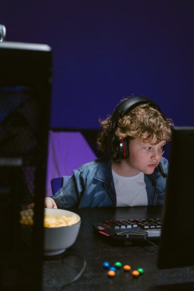 Ein Junge sitzt mit Kopfhörern vor einem Computerbildschirm mit einer Schüssel Chips
