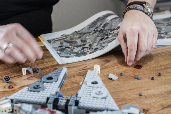 Eine Person schaut sich eine Anleitung an. Vor ihr liegen ein angefangenes LEGO Modell und weitere Bausteine.