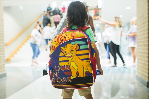 Ein Kind trägt einen riesigen Schulranzen mit Simba-Motiv in der Schule auf dem Rücken. 