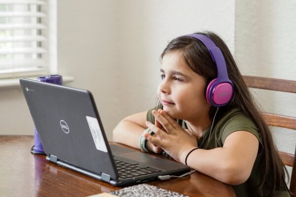 Mädchen mit Kopfhörern sitzt vor einem Laptop