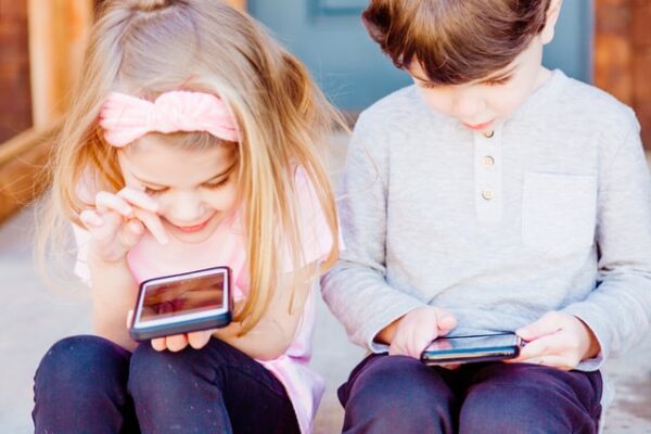 Zwei Kinder sitzen und halten beide ein Smartphone in der Hand