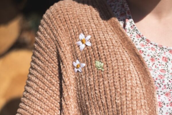 Eine braune Strickjacke mit zwei kleinen weißen Blumen und einem grünen Blatt darauf