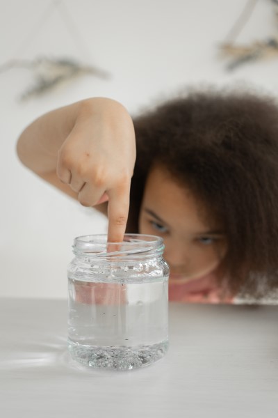Ein Mädchen rührt mit dem Finger in einem Glas voller Flüssigkeit