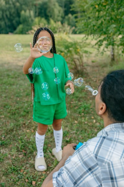 Ein Mädchen zerplatzt die Seifenblasen, die ihr Vater pustet