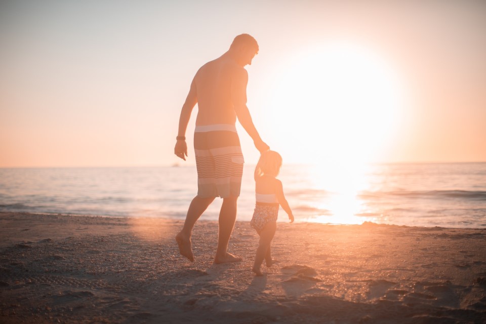 Ein Mann geht mit seiner Tochter beim Sonnenuntergang am Strand entlang