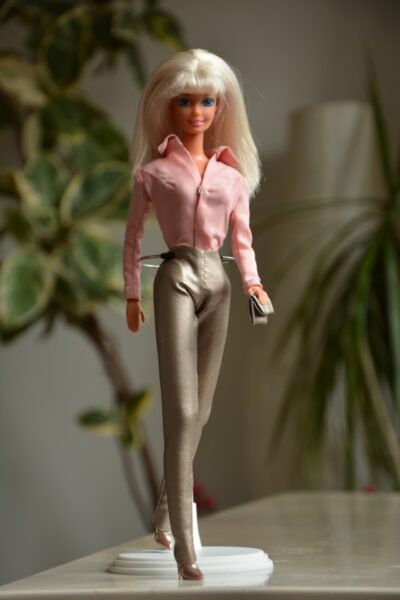 Eine blonde Barbie in einer pinken Bluse und grünen Hose. 