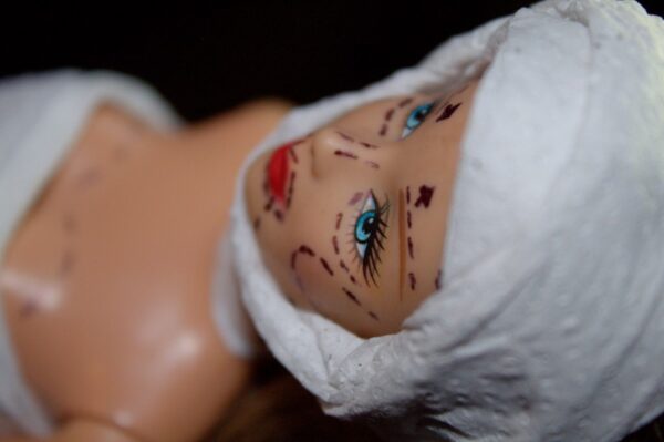 Eine Barbie hat auf dem Gesicht Linien zur Vorbereitung einer Schönheits-OP.