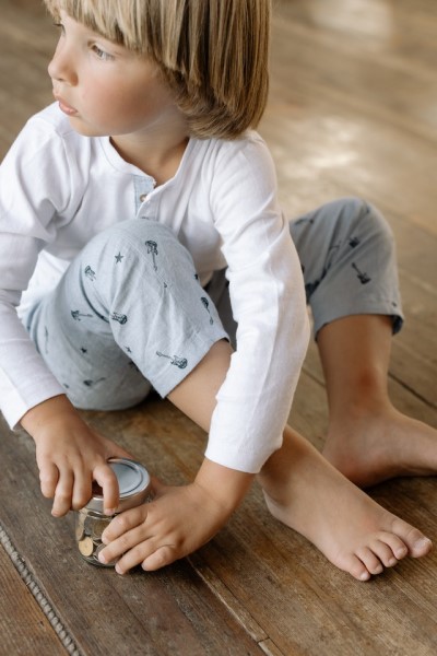 Kind sitzt auf Holzboden und hat Glas mit Münzen in der Hand.