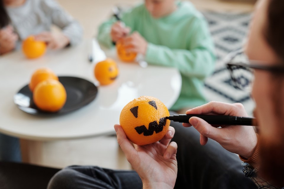 Eine Familie malt zusammen Orangen mit Kürbisfratzen an.