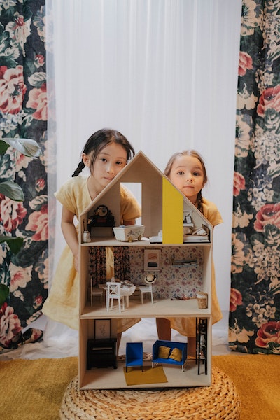 Zwei Kinder stehen hinter einem minimalistischen möblierten Puppenhaus.