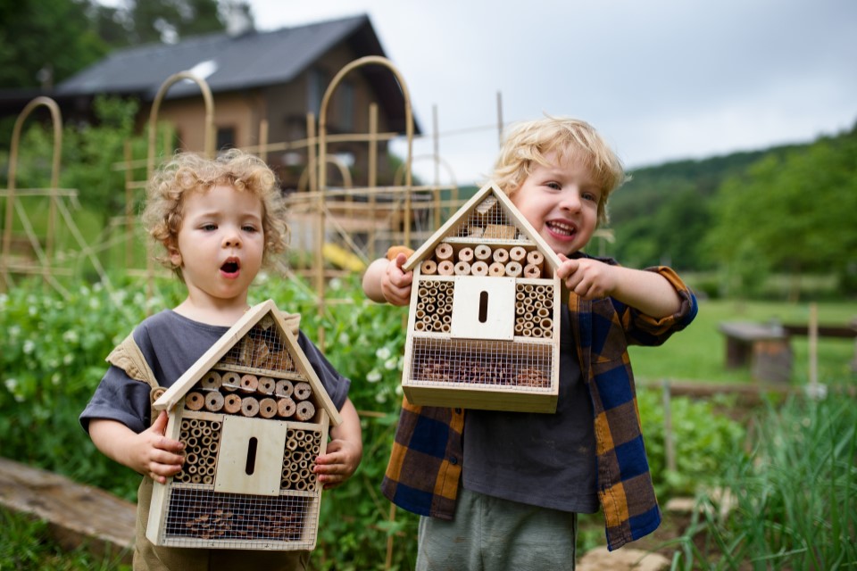 Zwei Kinder stehen im Garten und halten ein Insektenhotel in den Händen.