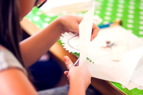 Ein Kind schneidet vorsichtig eine Form aus weißem Papier aus. 