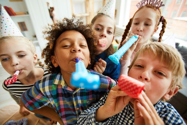 Mehrere Kinder haben Party-Tröten im Mund.