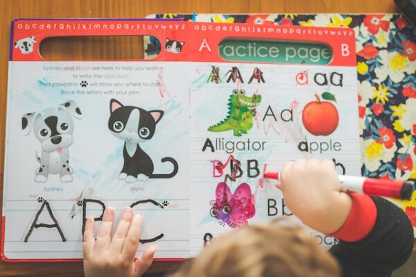 Ein Kind malt in einem Buch, das mit Bildern die Buchstaben beibringt. 